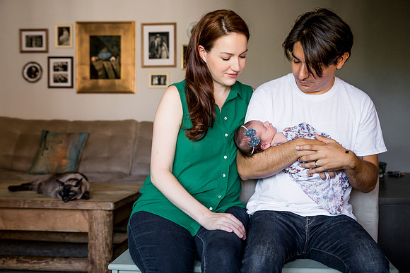 Mother and father hold their newborn baby girl. Cat lounges in the background